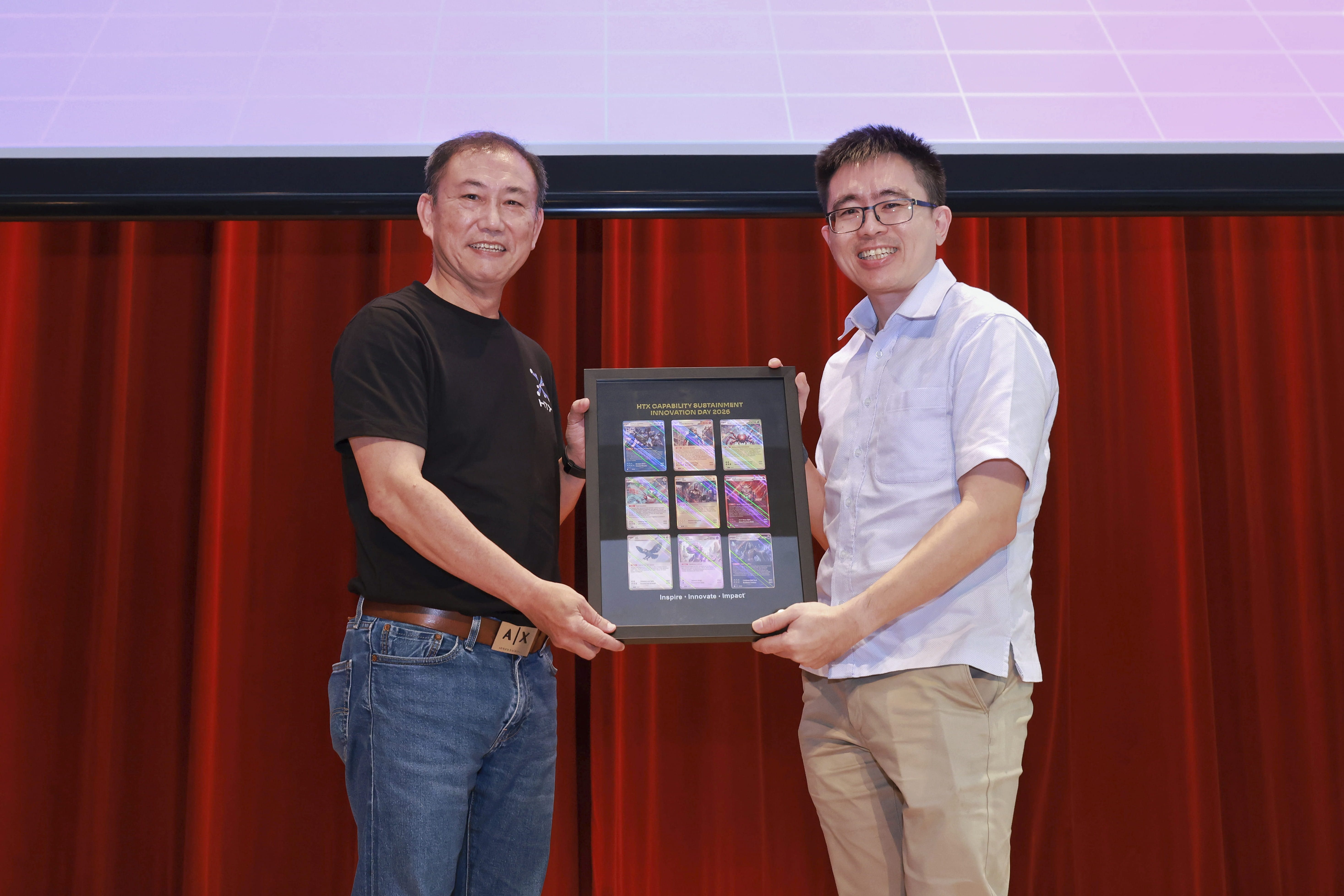 Two men posing with a framed display on stage.