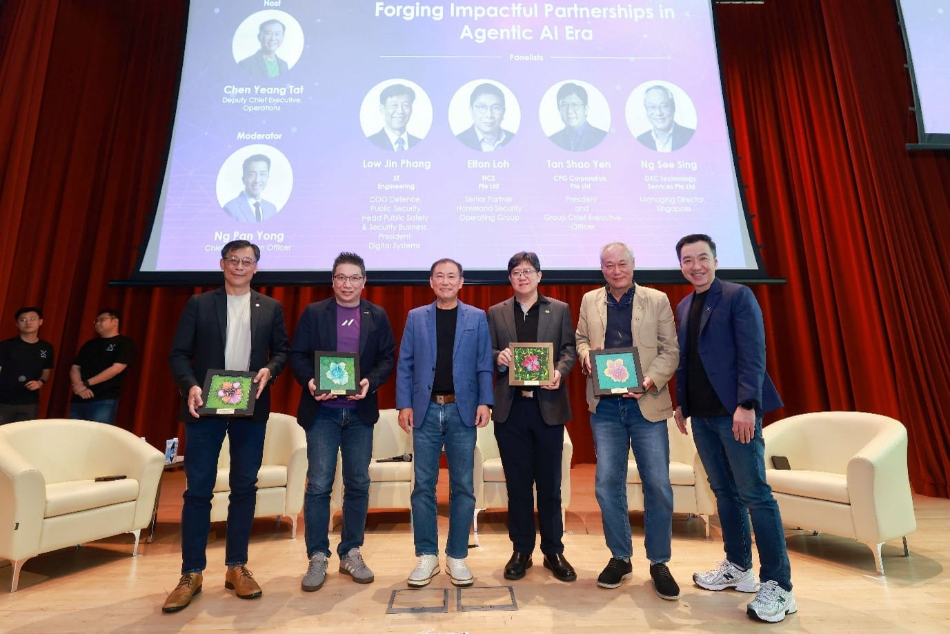 Six men standing on stage, with four holding framed items.