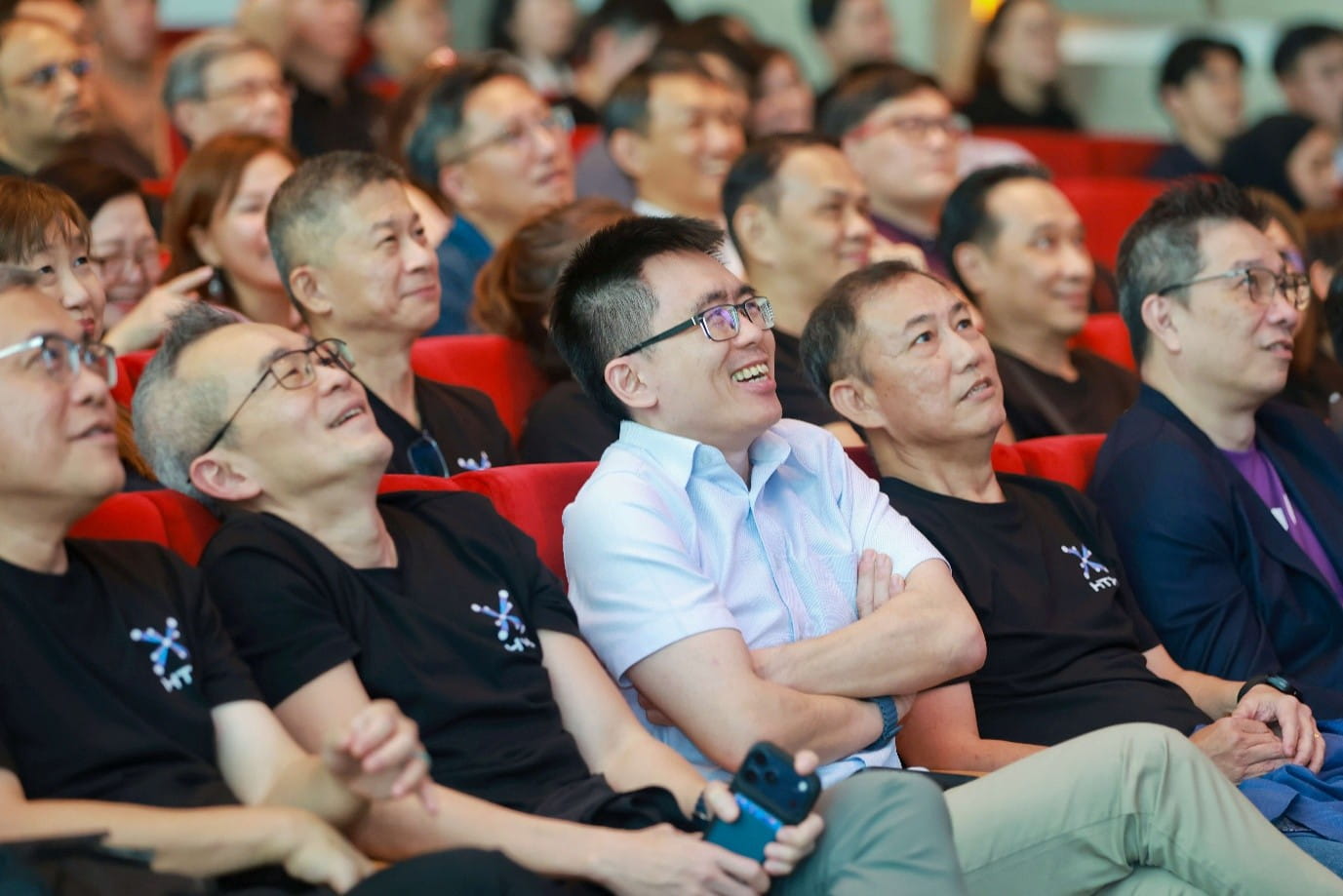 Audience seated in red auditorium chairs.