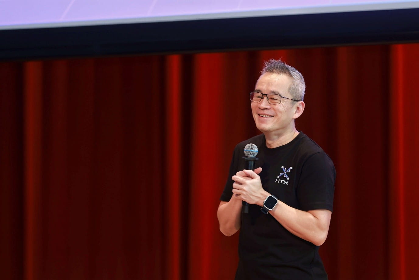 Smiling man holding a microphone on stage.