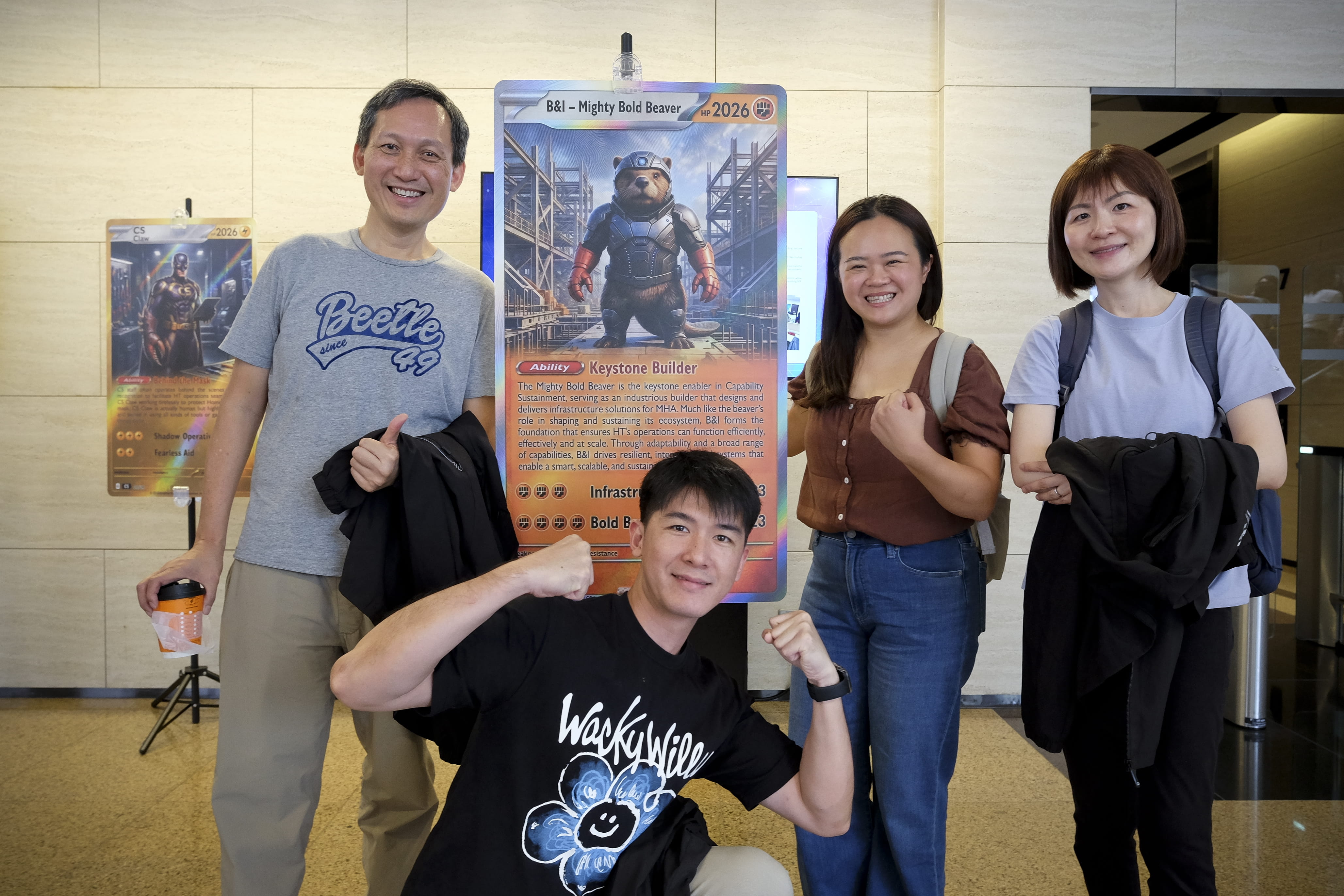 Four people posing indoors beside a "B&I - Mighty Bold Beaver" character poster.