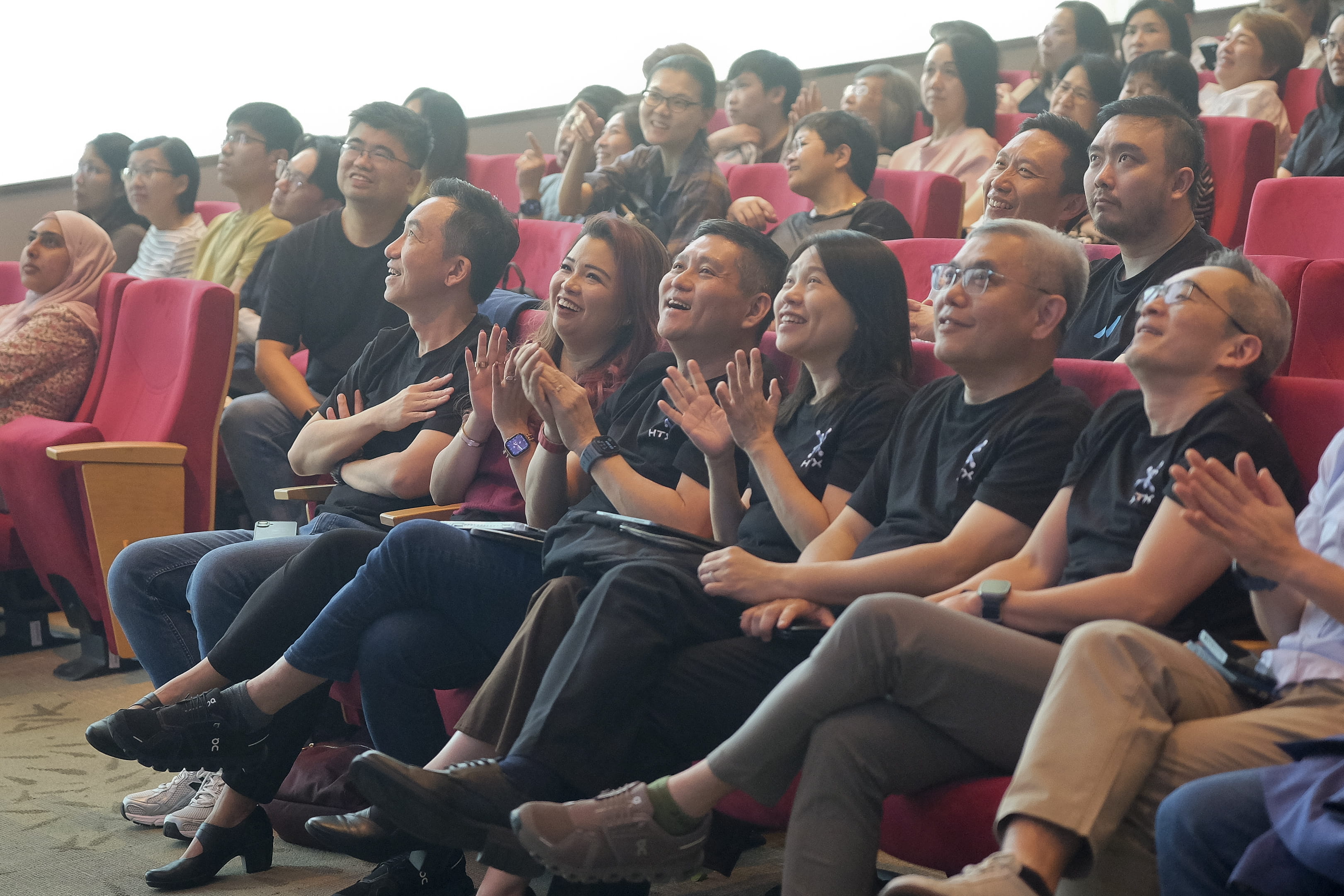 Audience seated in an auditorium, reacting enthusiastically during a presentation.