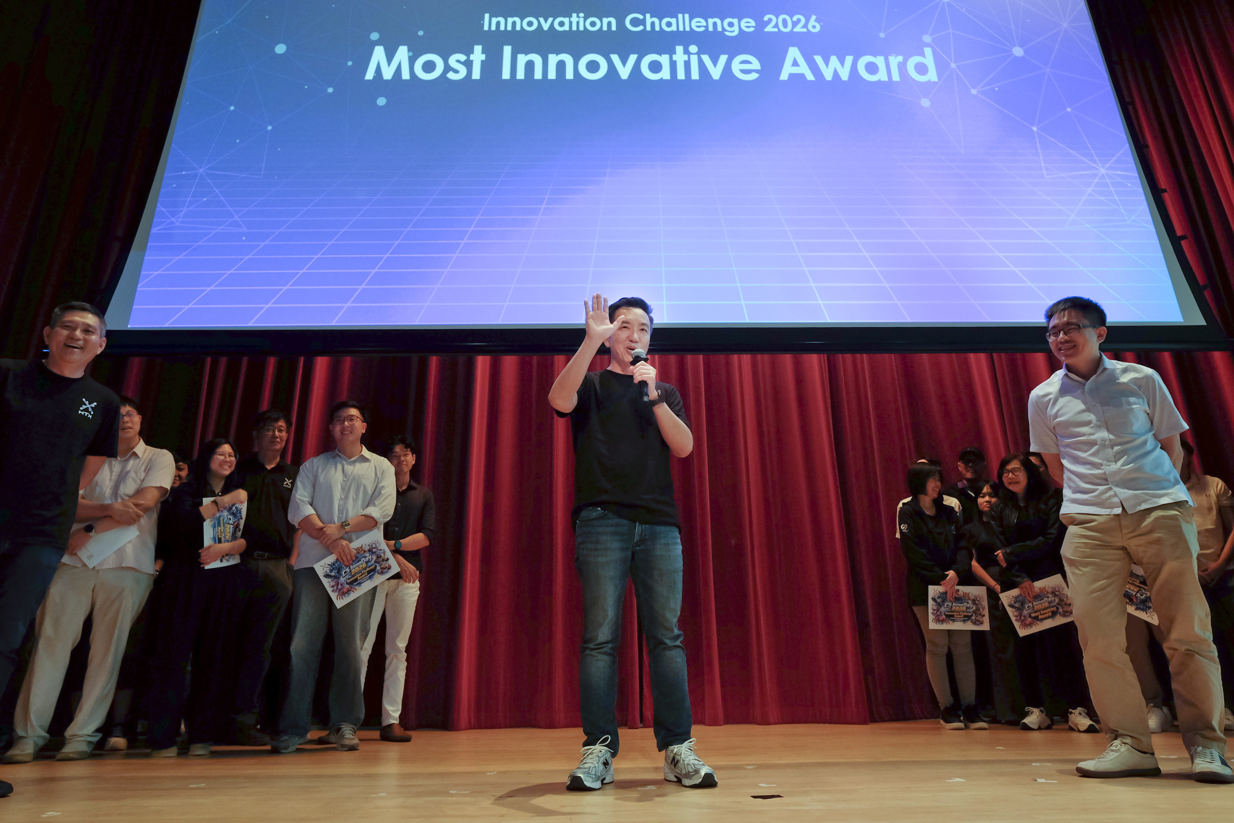 Speaker holding a microphone beneath a screen labelled “Innovation Challenge 2026: Most Innovative Award.”