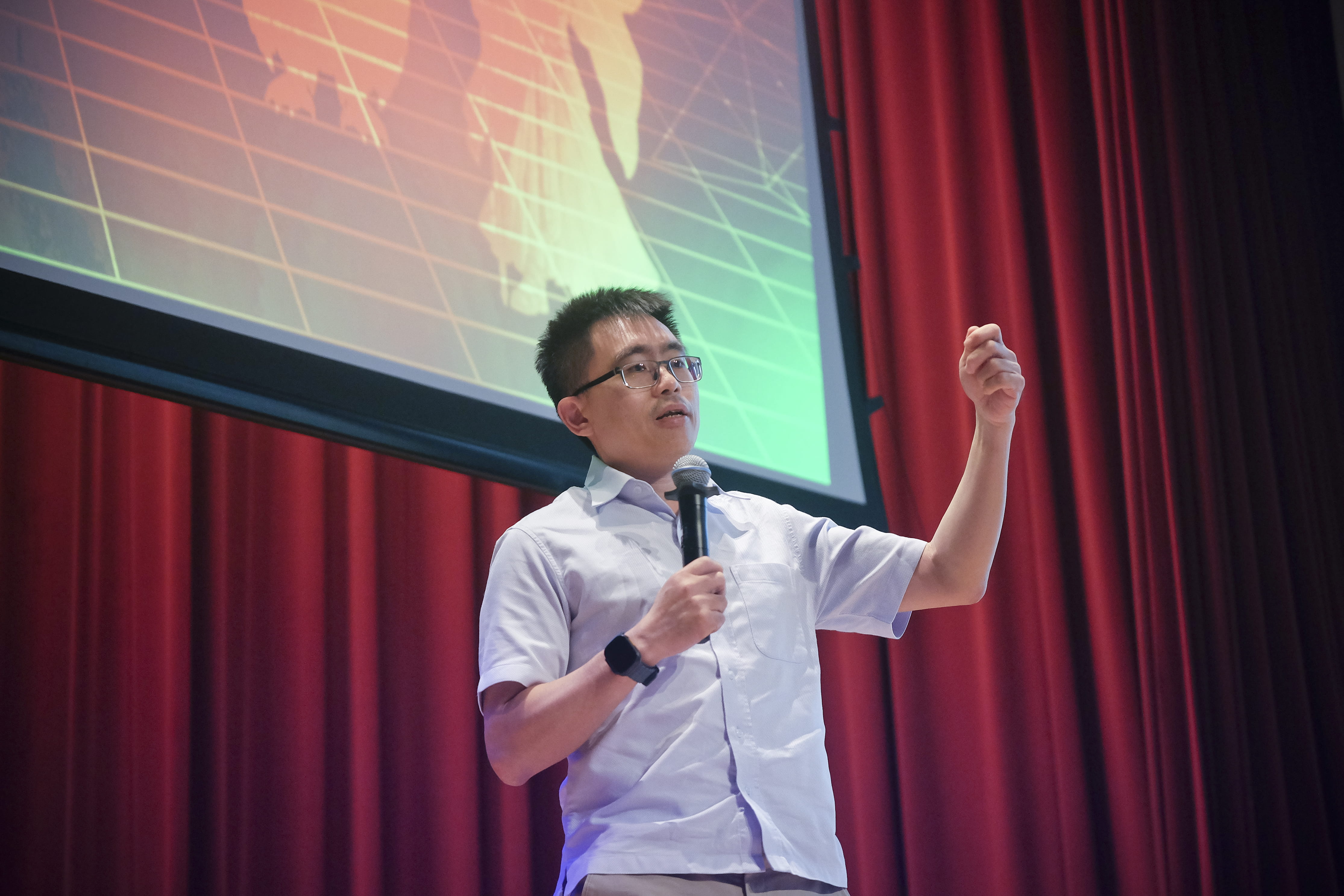 Male presenter holding a microphone and gesturing on stage during a talk.