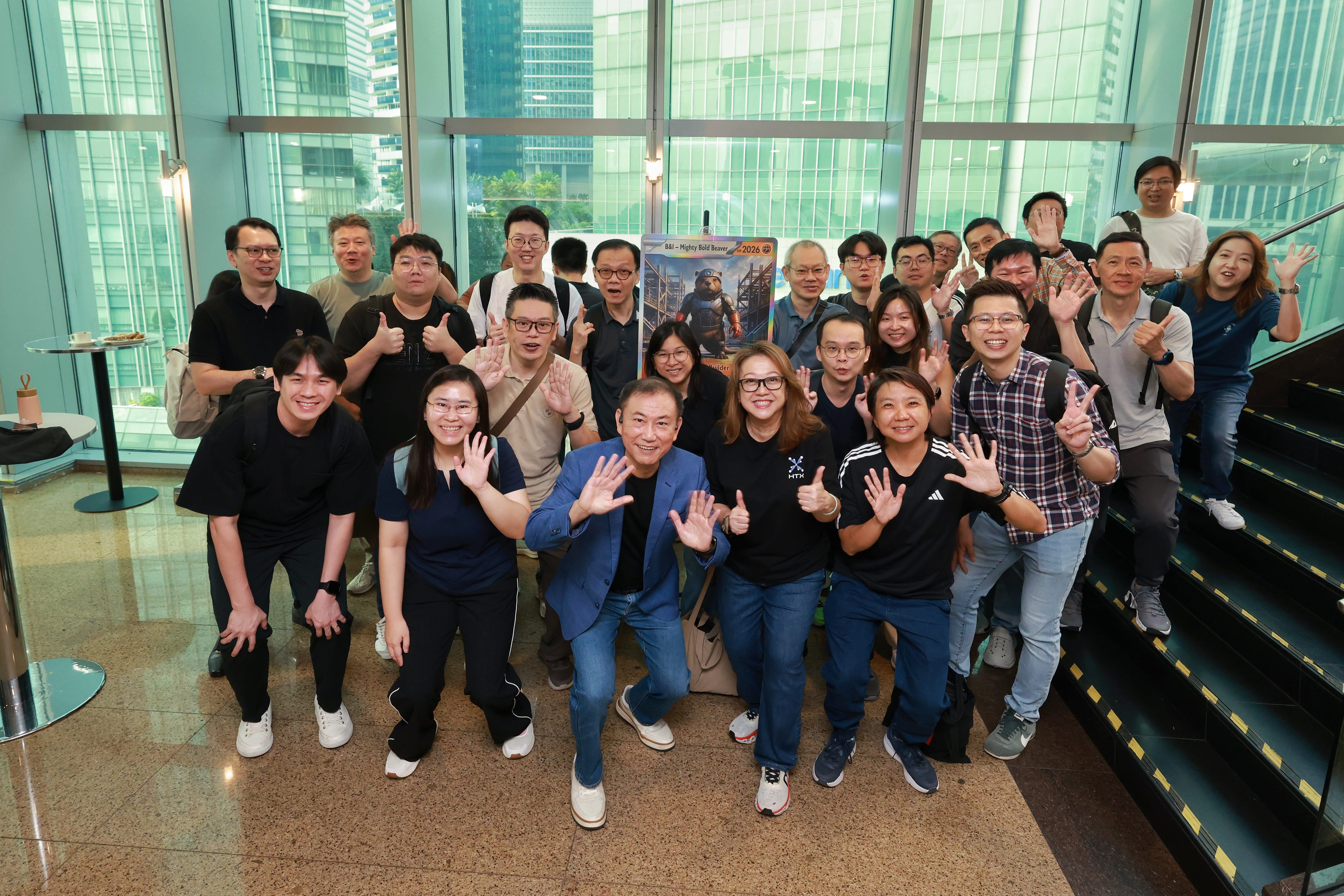 Large group of adults posing and waving inside a modern building.