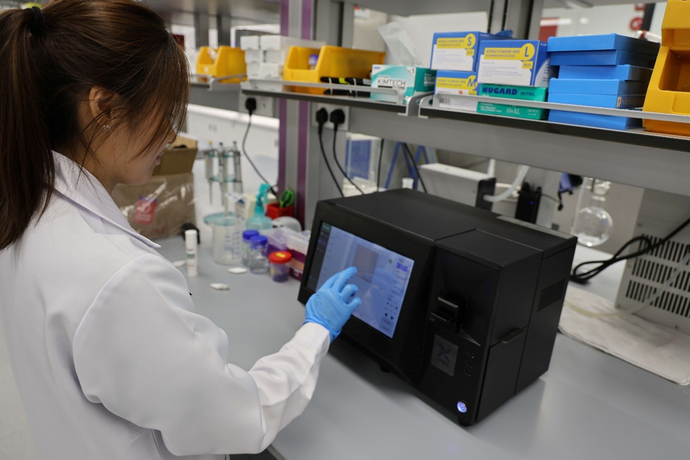 Lab worker using a touchscreen device with medical supplies nearby.