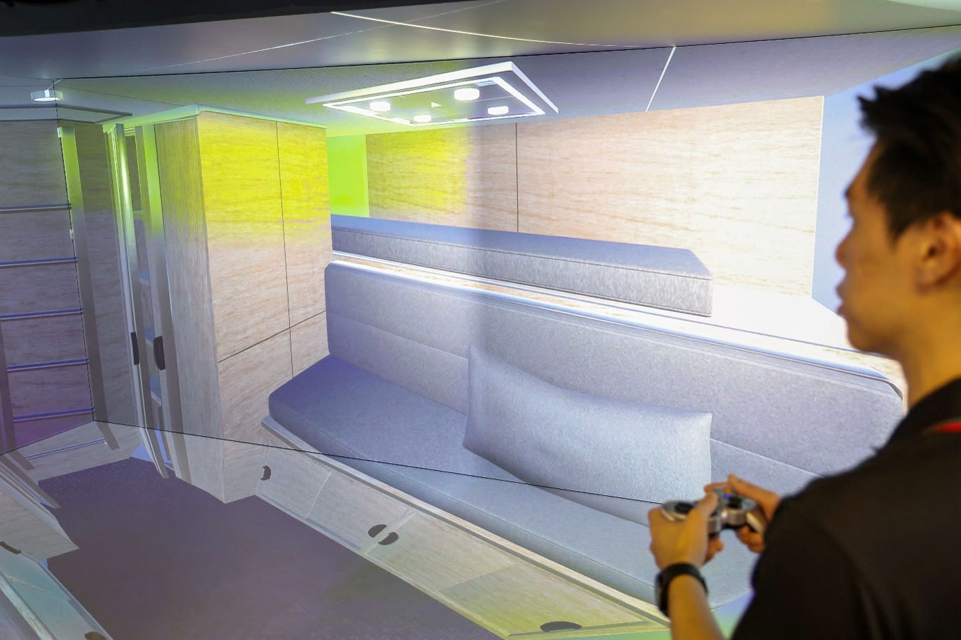 Person operating a handheld controller, viewing a 3D-rendered boat interior.
