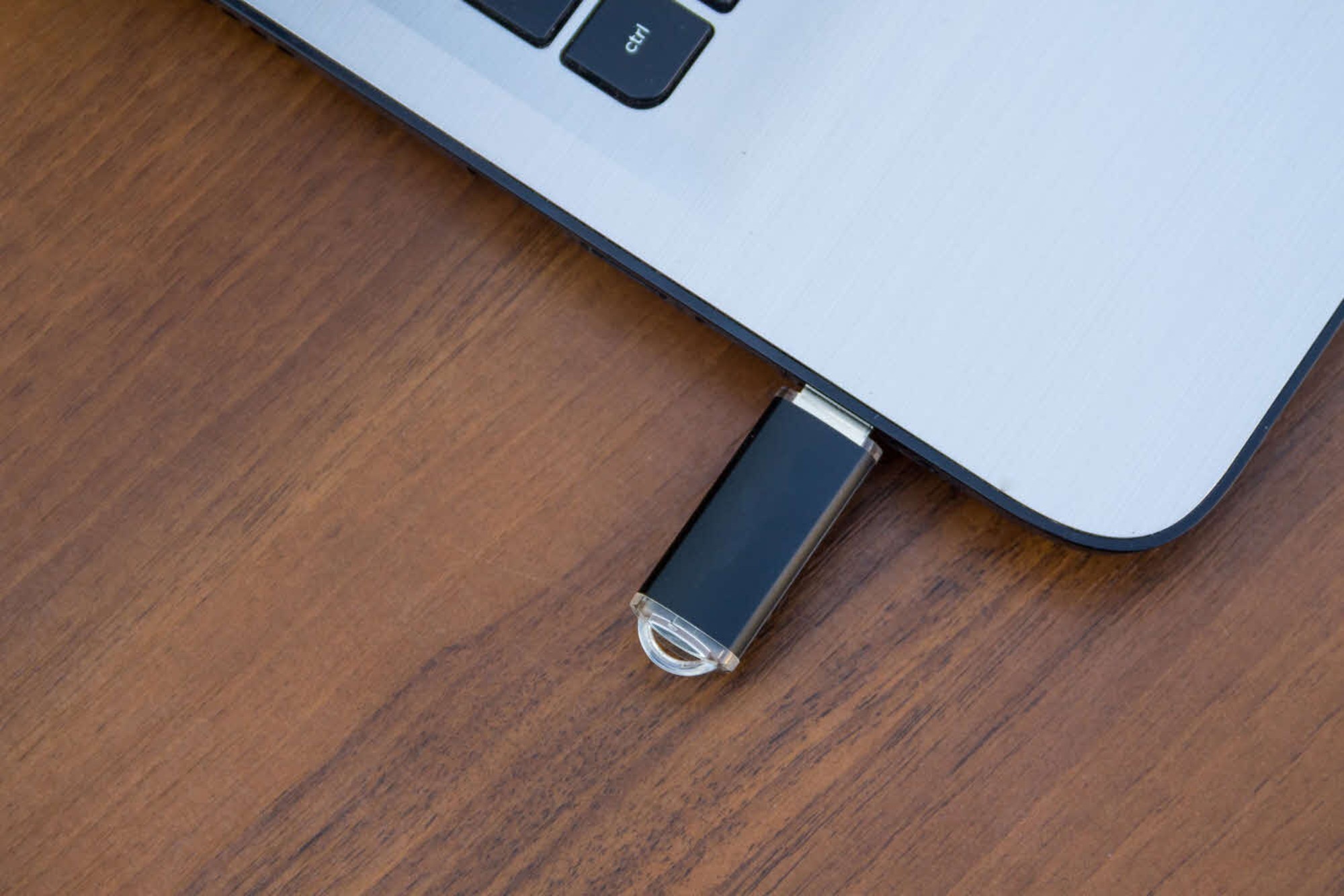 A black USB flash drive plugged into a silver laptop on a wooden surface.
