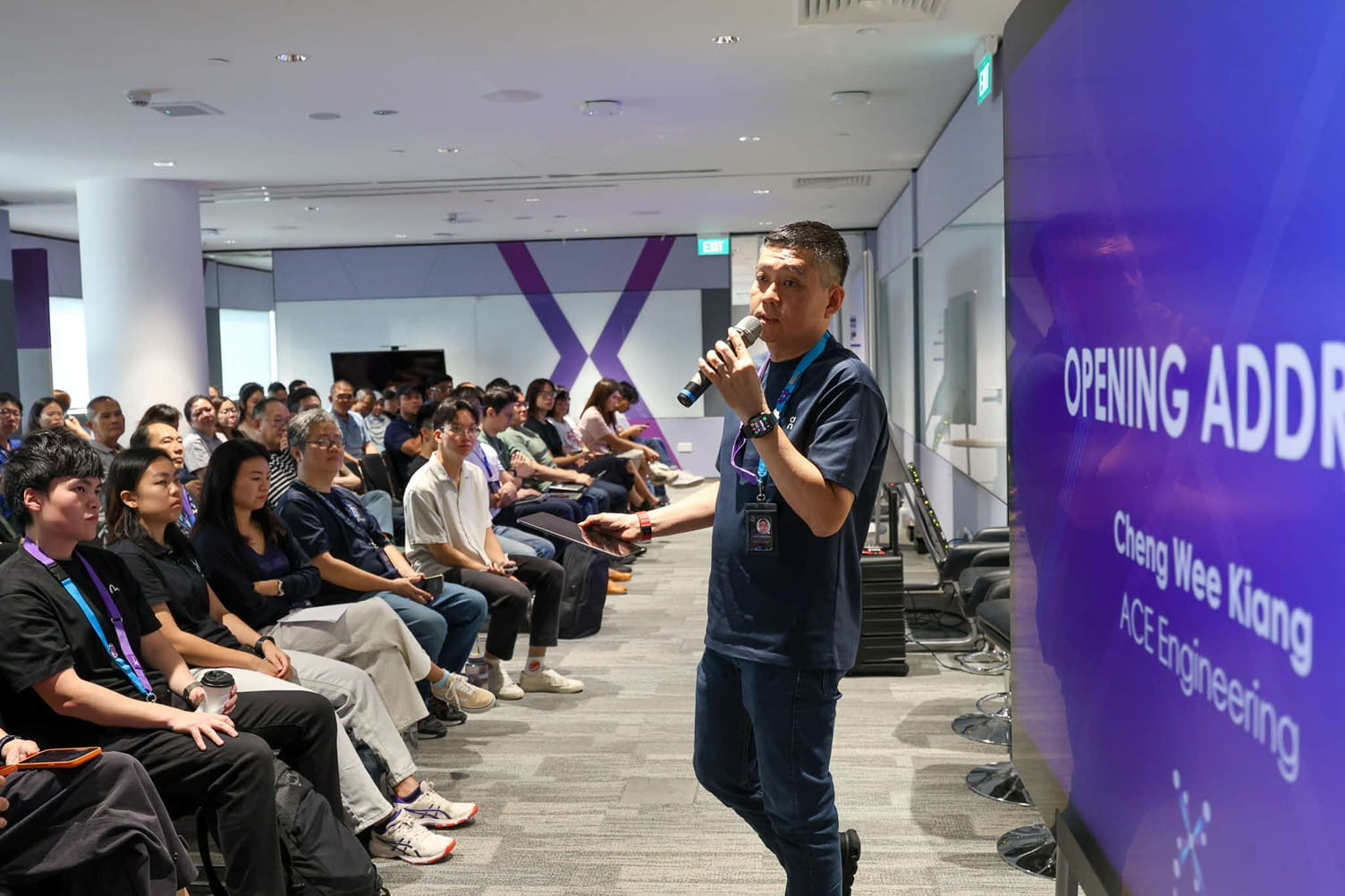 A male speaker giving an opening address to an audience seated in a conference room.