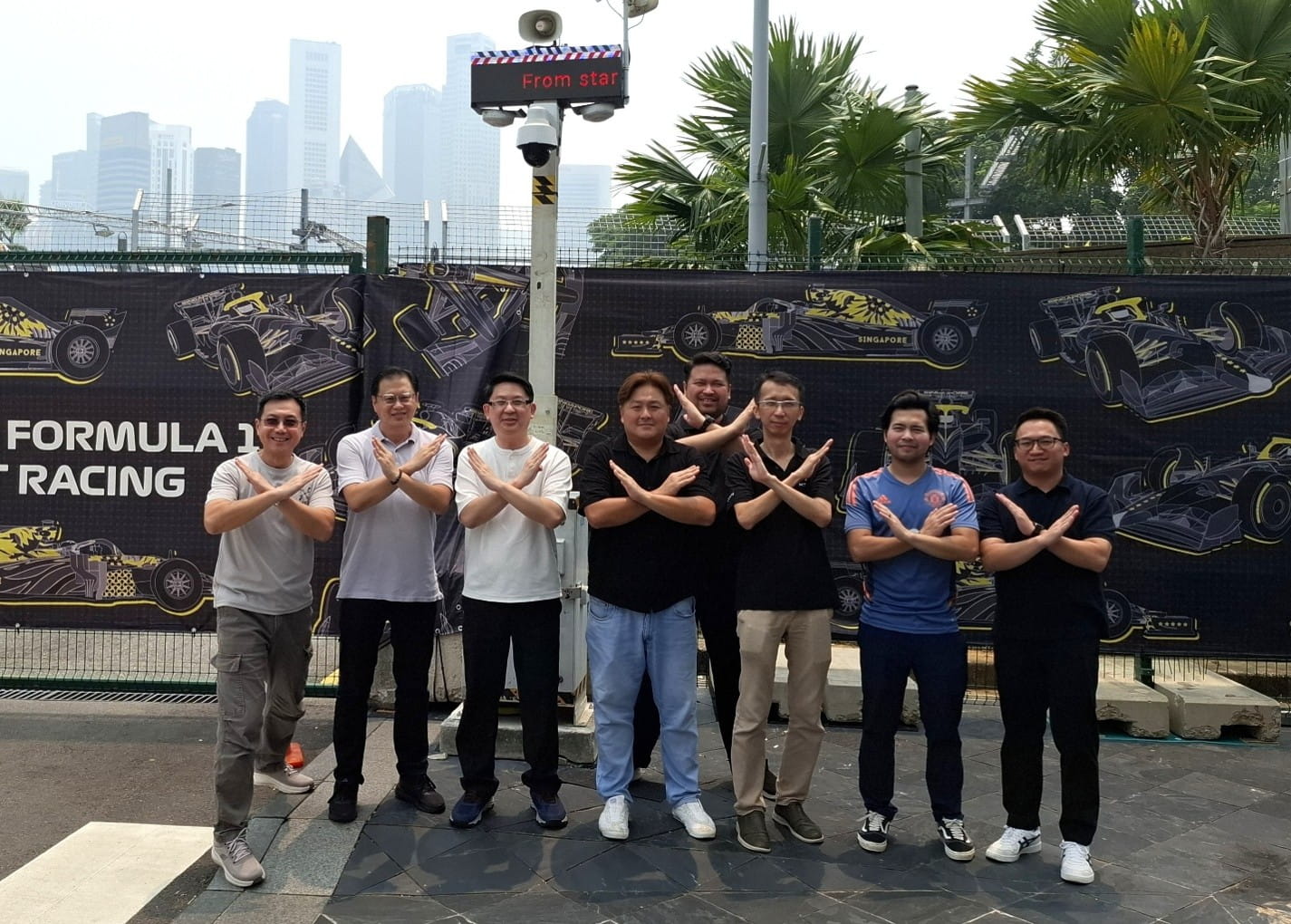 Group of adults posing outside a F1 racing venue.