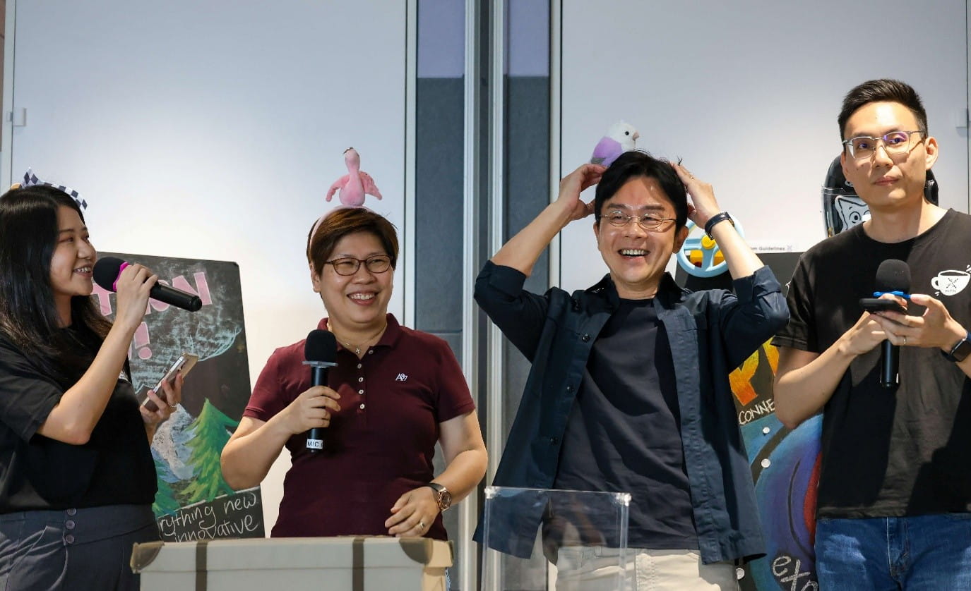 Two people participating in a lively indoor activity, with two emcees by their side.