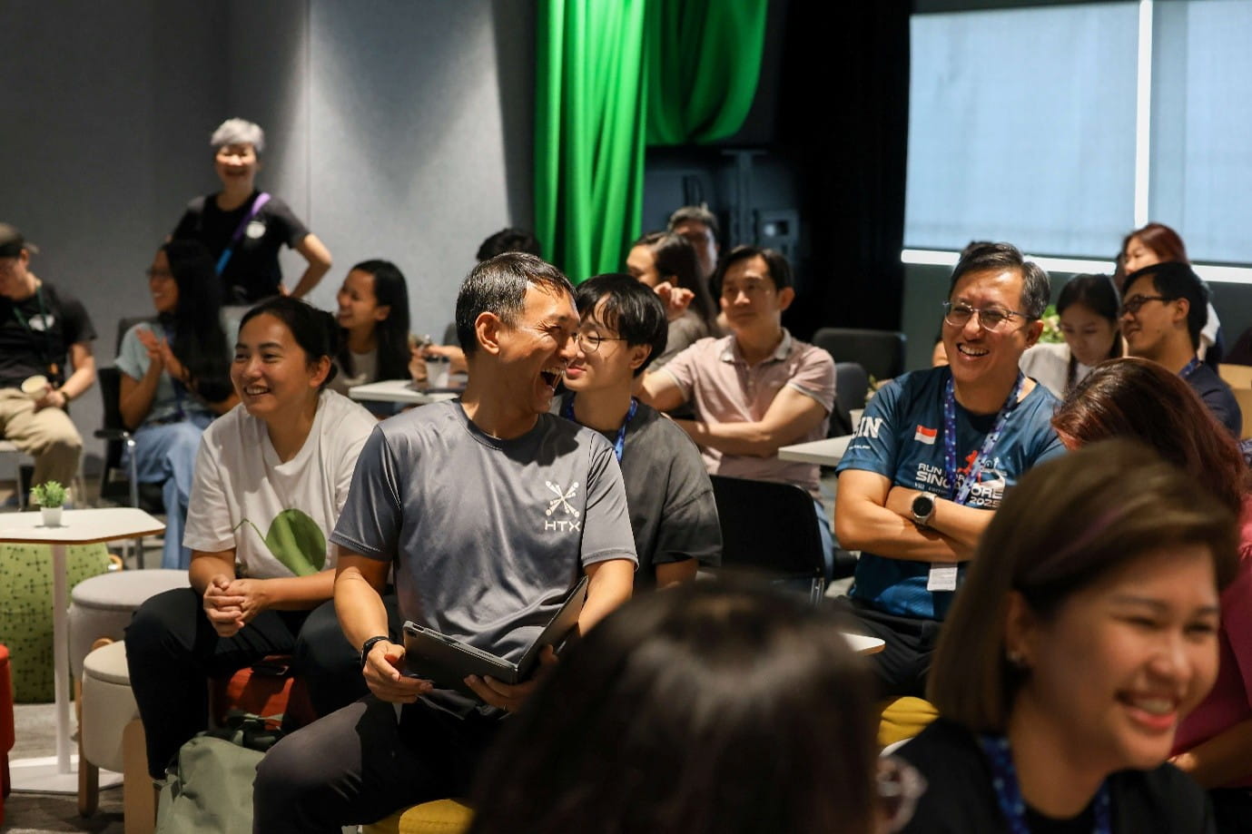 Audience seated for an indoor event, smiling and conversing among tables.