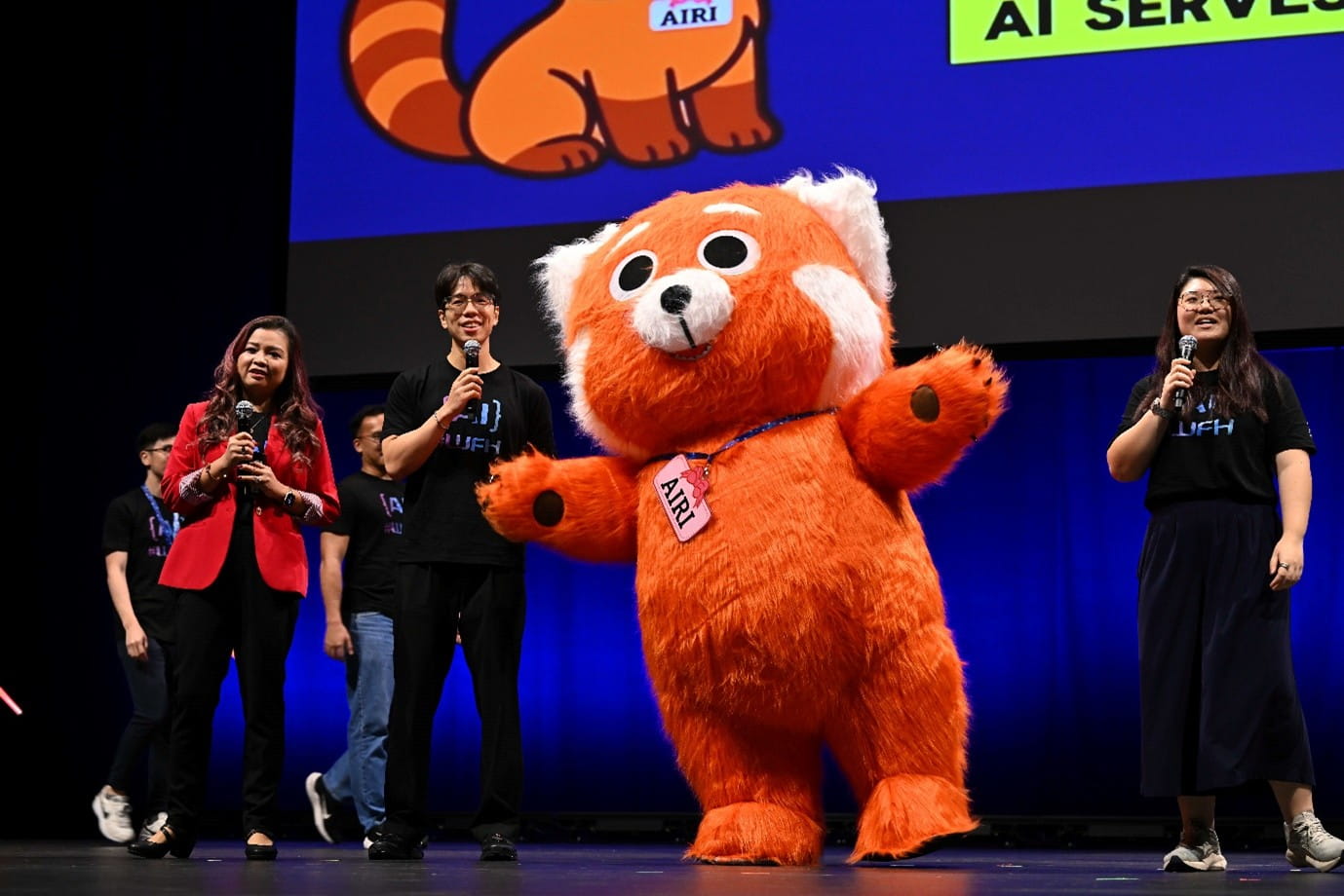 A large orange mascot and three people on stage.