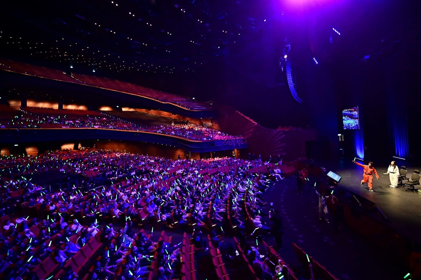 Large audience holding glowing light sticks during a live performance on stage.