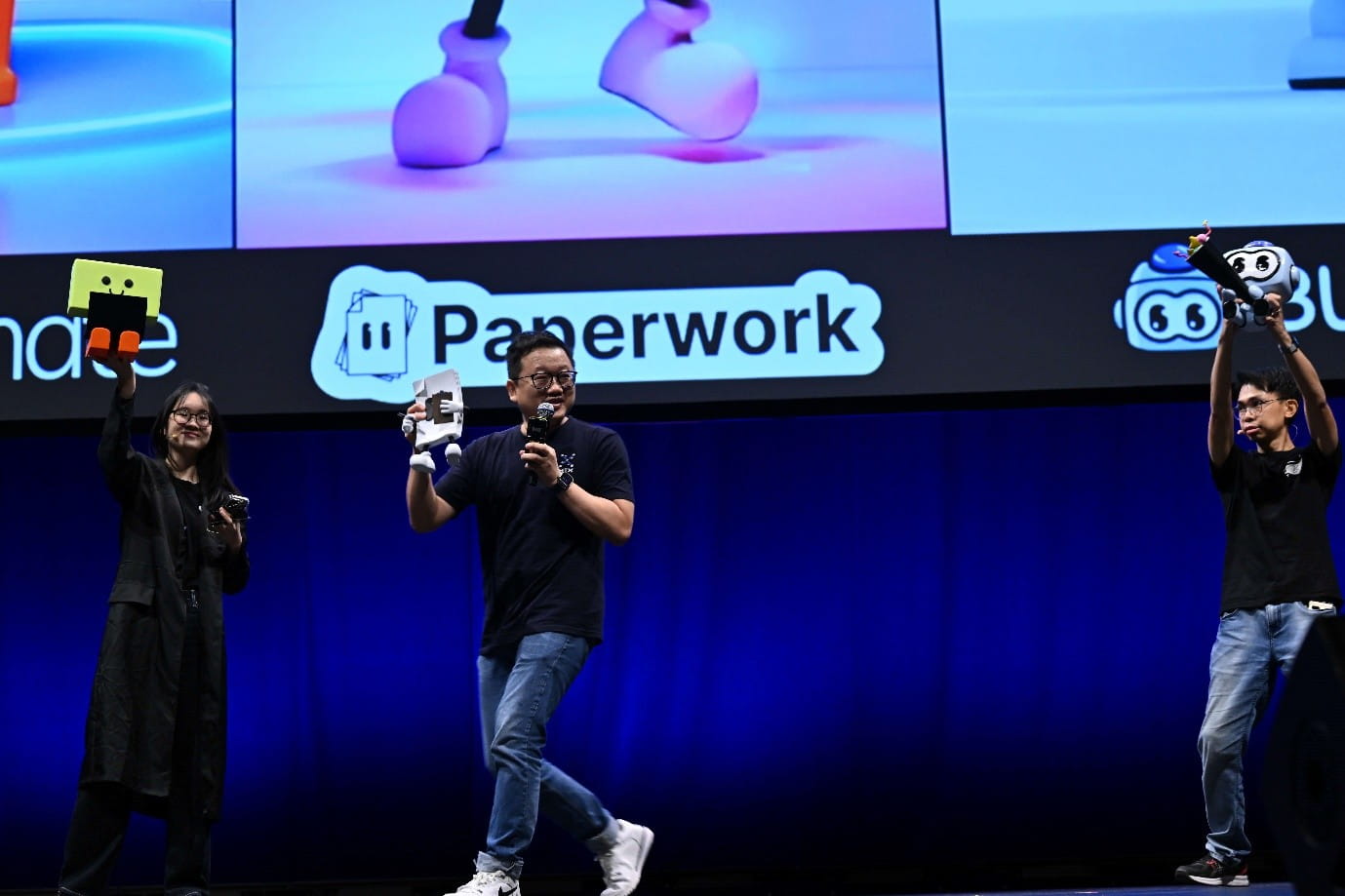 Three people on stage presenting apps, with a large screen behind them displaying app icons and names.