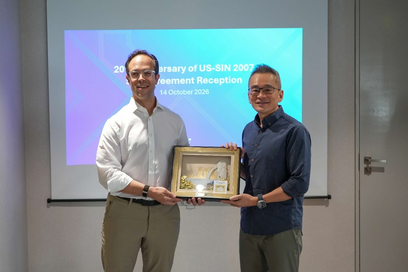 Two men presenting a framed commemorative artwork during a reception.