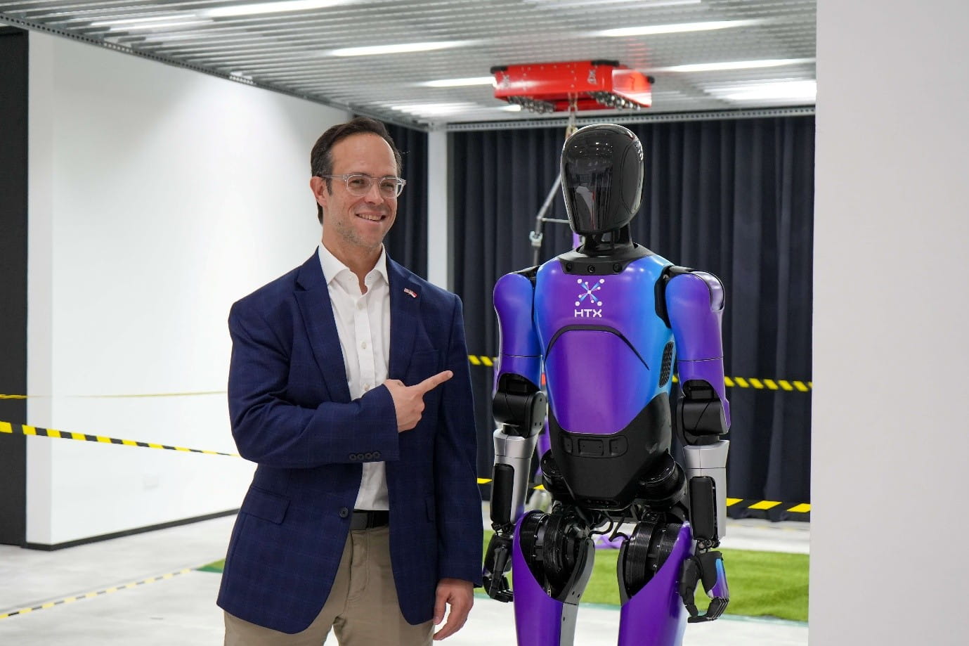 A man standing beside and pointing towards a humanoid robot.