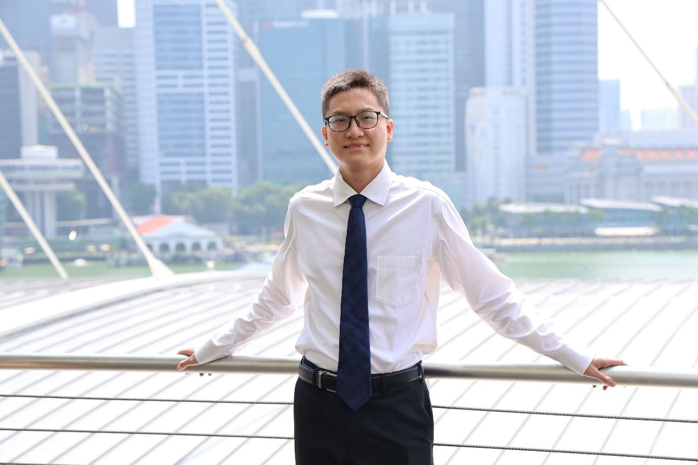 A young man posing outdoors with a city skyline in the background.
