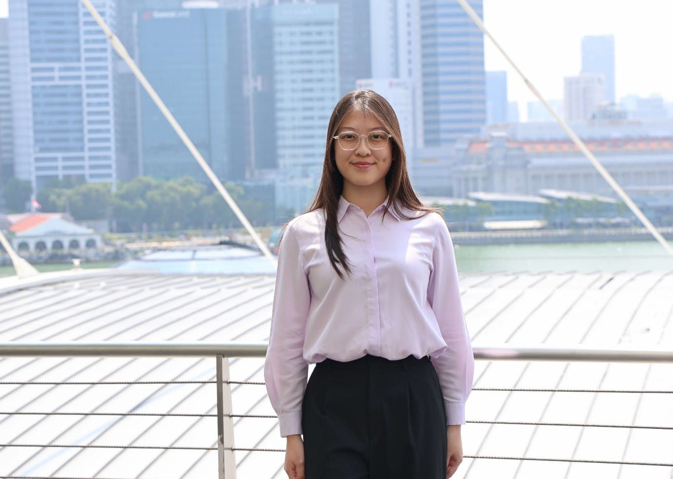 A young woman posing outdoors with a city skyline in the background.