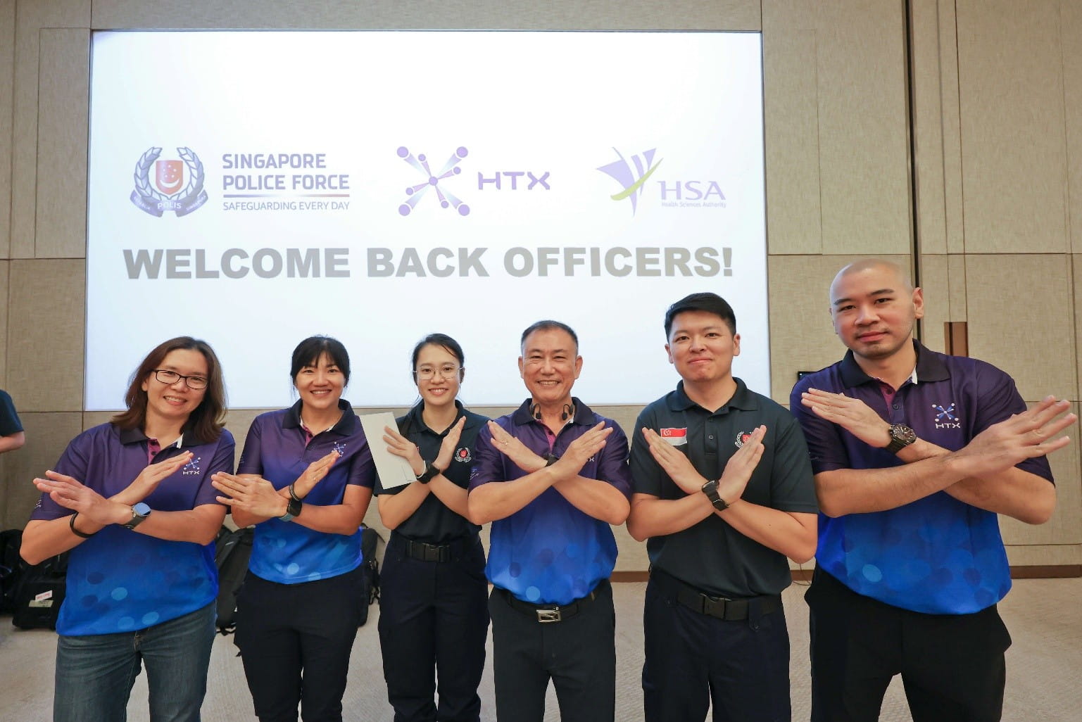 Six officers posing with crossed arms, with a backdrop slide reading "Welcome back officers!" and displaying SPF, HTX, and HSA logos.
