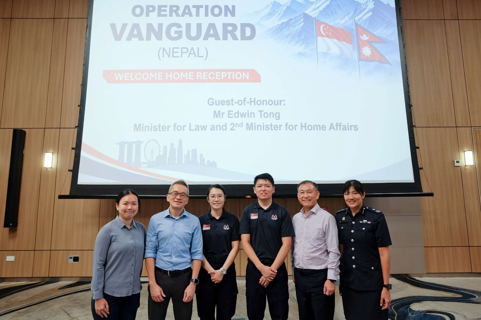 Six people posing in front of a presentation screen during the Operation Vanguard (Nepal) welcome-home reception.