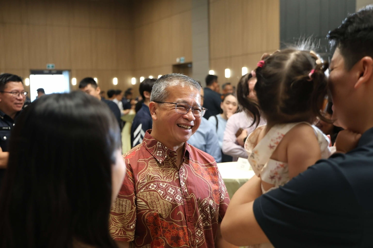 An older man smiling while looking at a father holding a young child.
