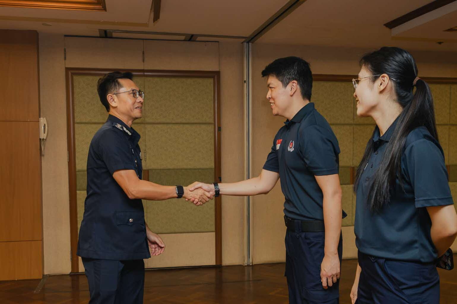 Two men shaking hands while a woman stands beside them in a conference room.