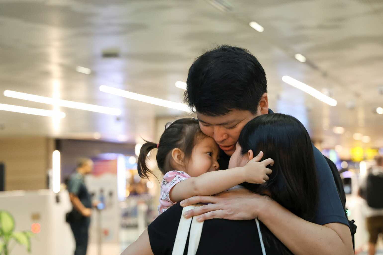 A family of 3 embracing inside an airport terminal.
