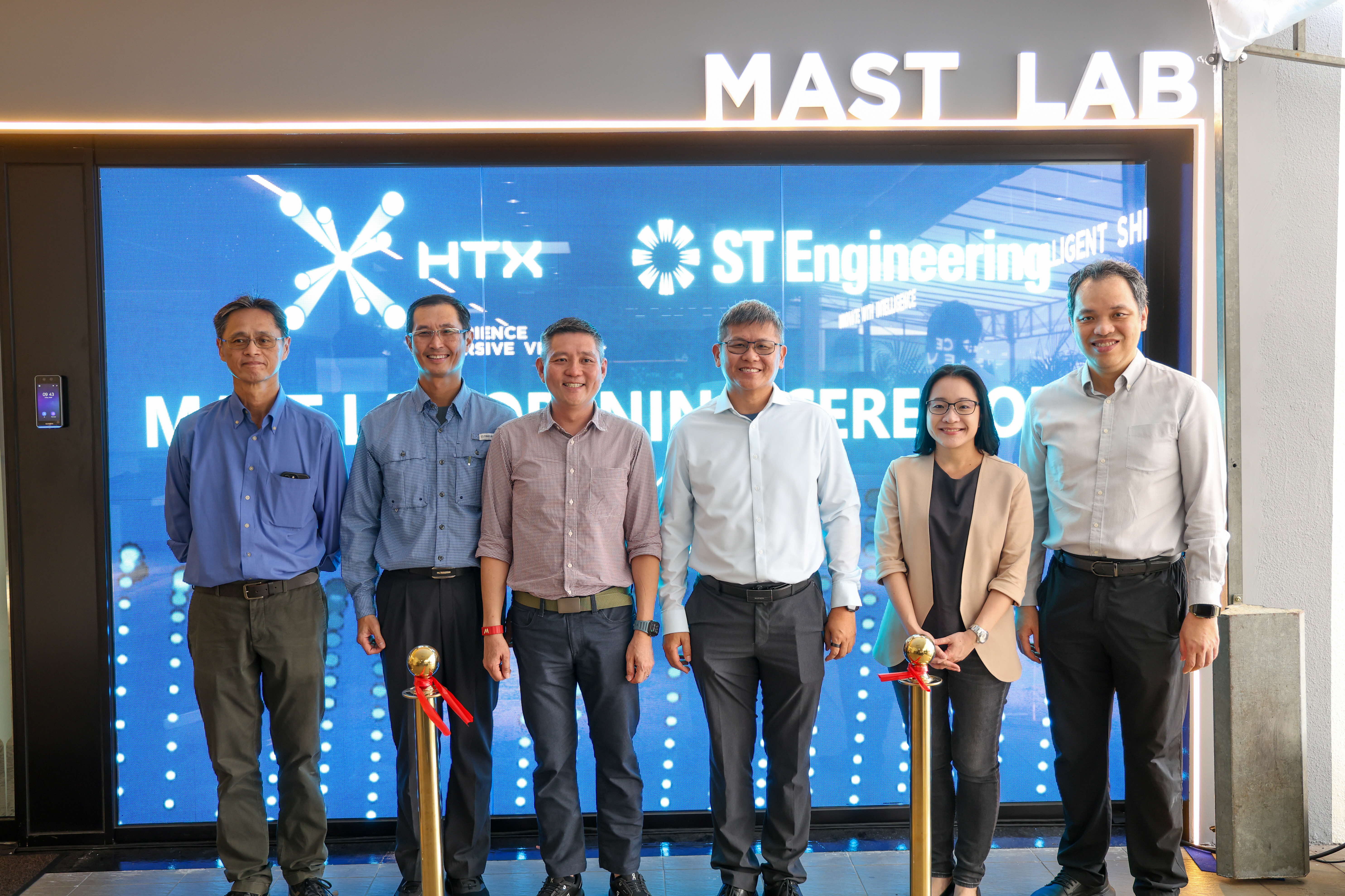 Six people standing in front of a digital display with logos of HTX and ST Engineering, at the opening of MAST Lab.