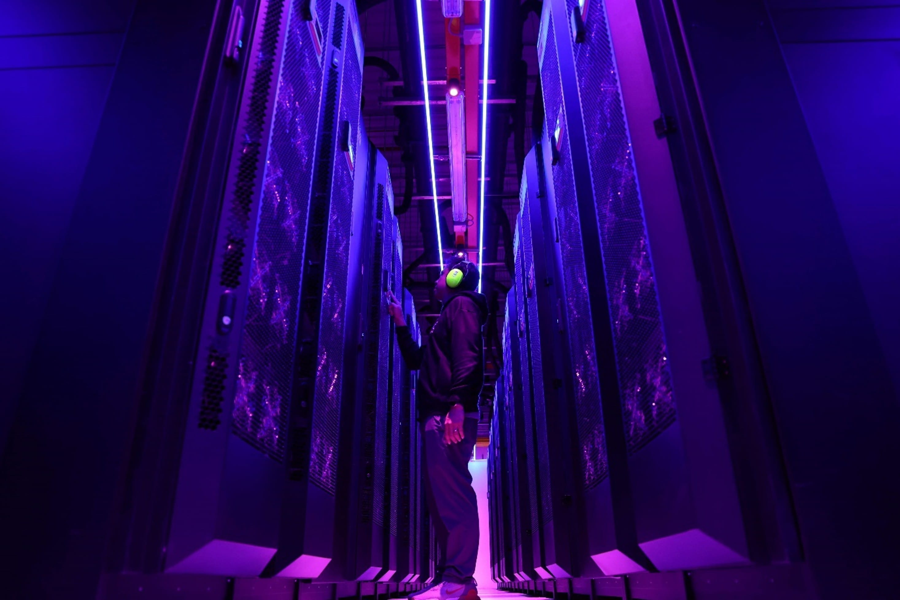 A person standing between rows of server racks in a server room.