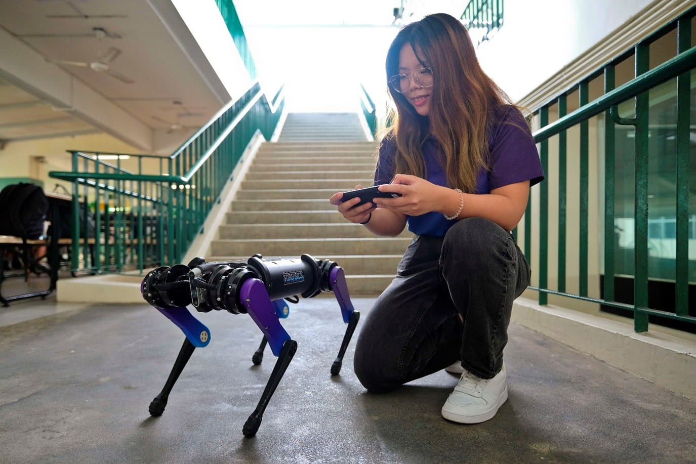 A woman kneeling on one knee while controlling a four-legged robot.