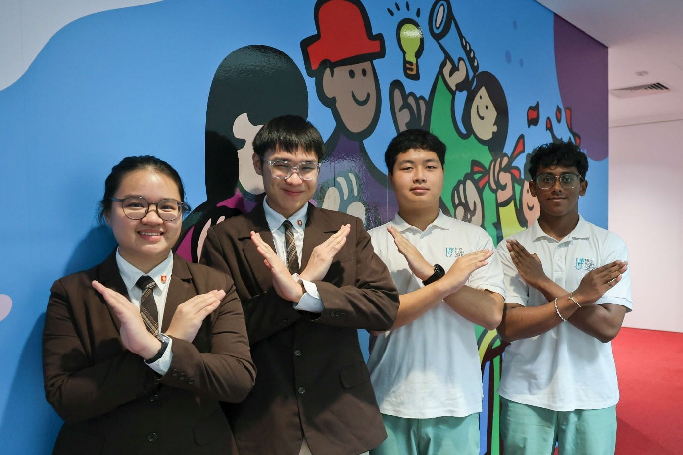 Four young people posing in front of a colourful cartoon mural indoors.