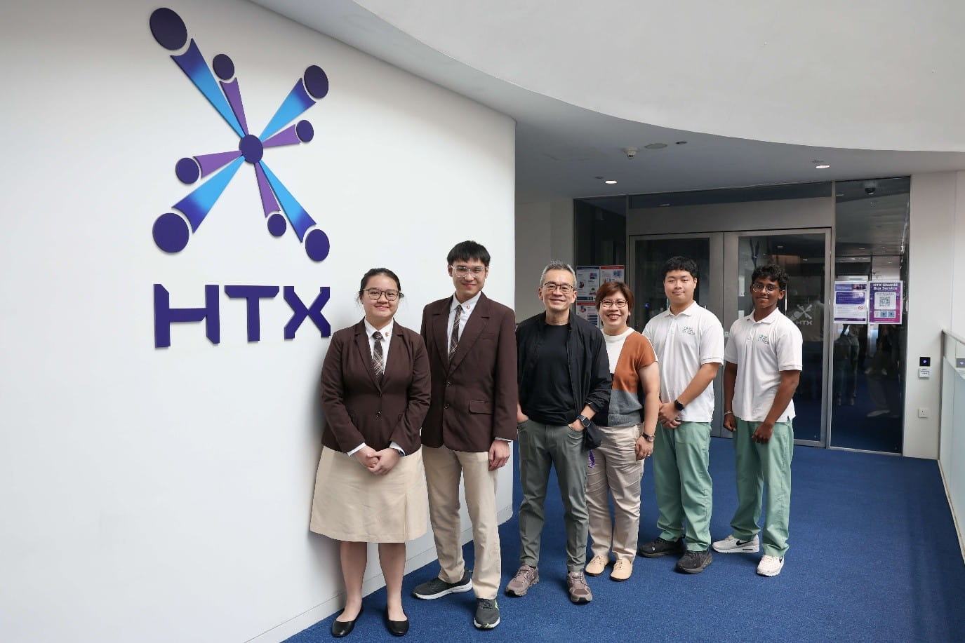 Six people posing beside the HTX logo on a wall.