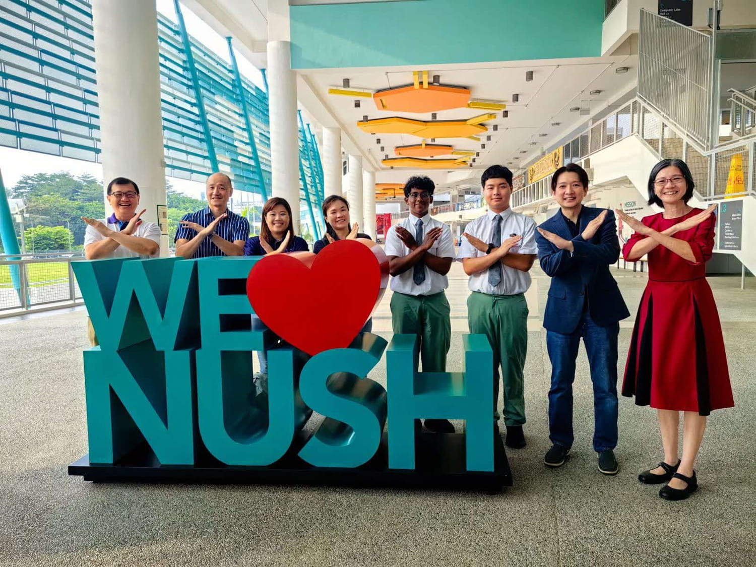 Eight people posing beside a large “WE ♥ NUSH” sign inside a building.