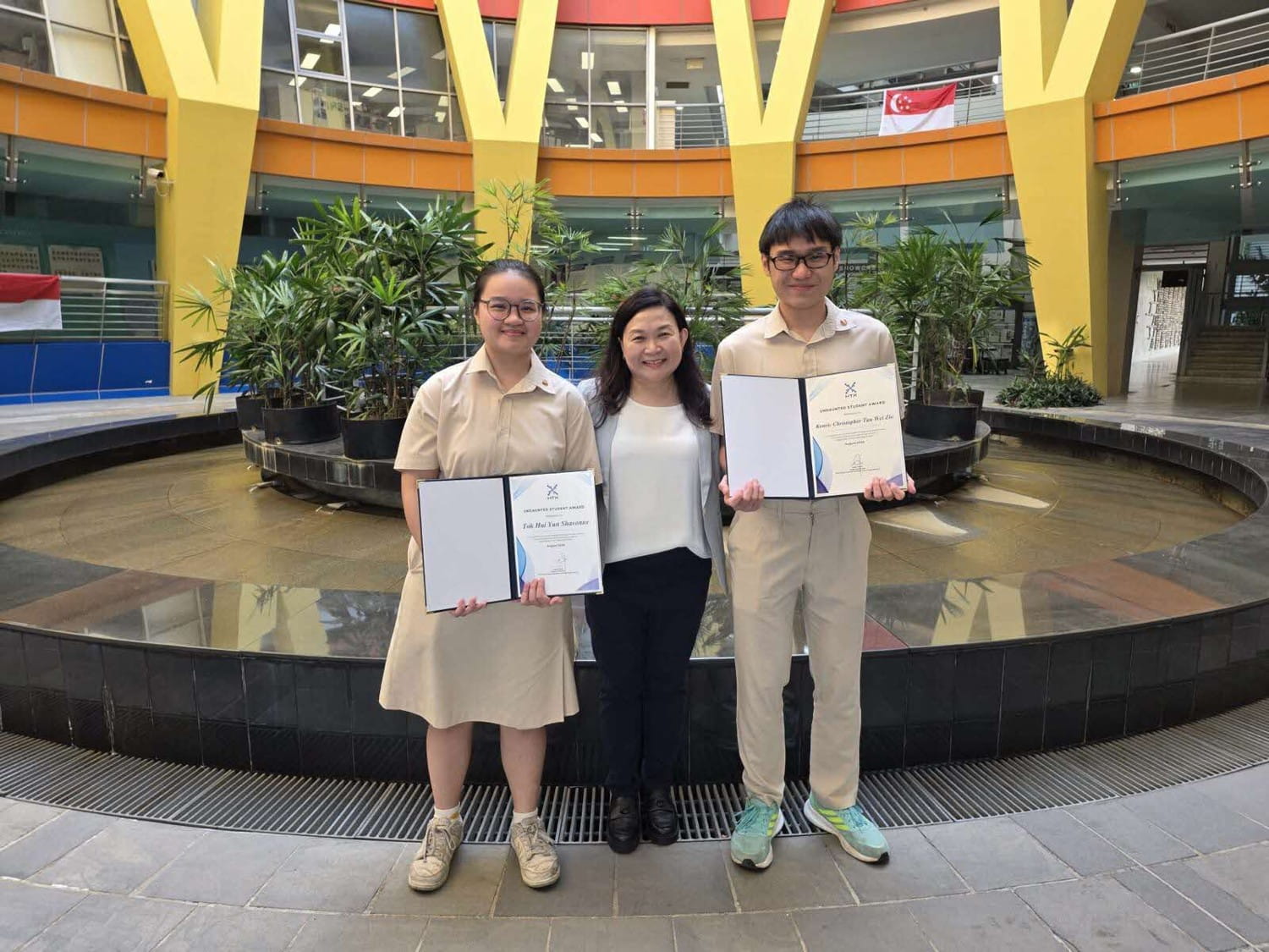 Three people posing, of which two are students holding certificates.