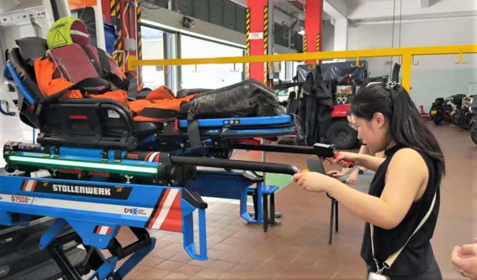 A woman operates a medical stretcher carrying a rescue mannequin in an indoor training facility.