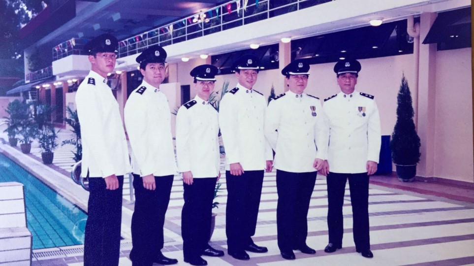 A group of six men in white uniforms with dark caps poses in a row.
