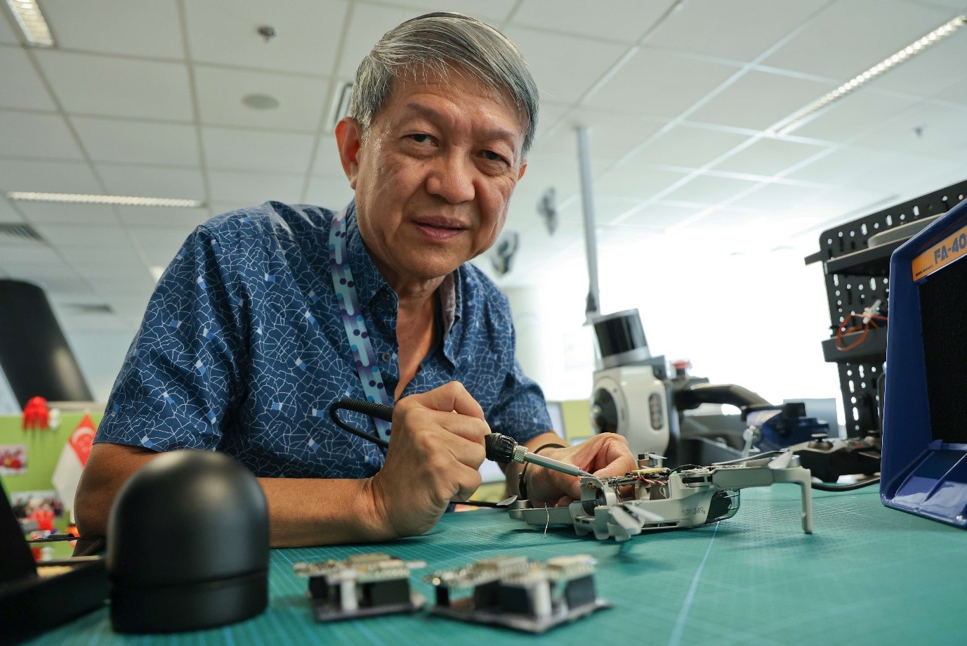 A man soldering a small drone component on a workbench in an indoor setting.