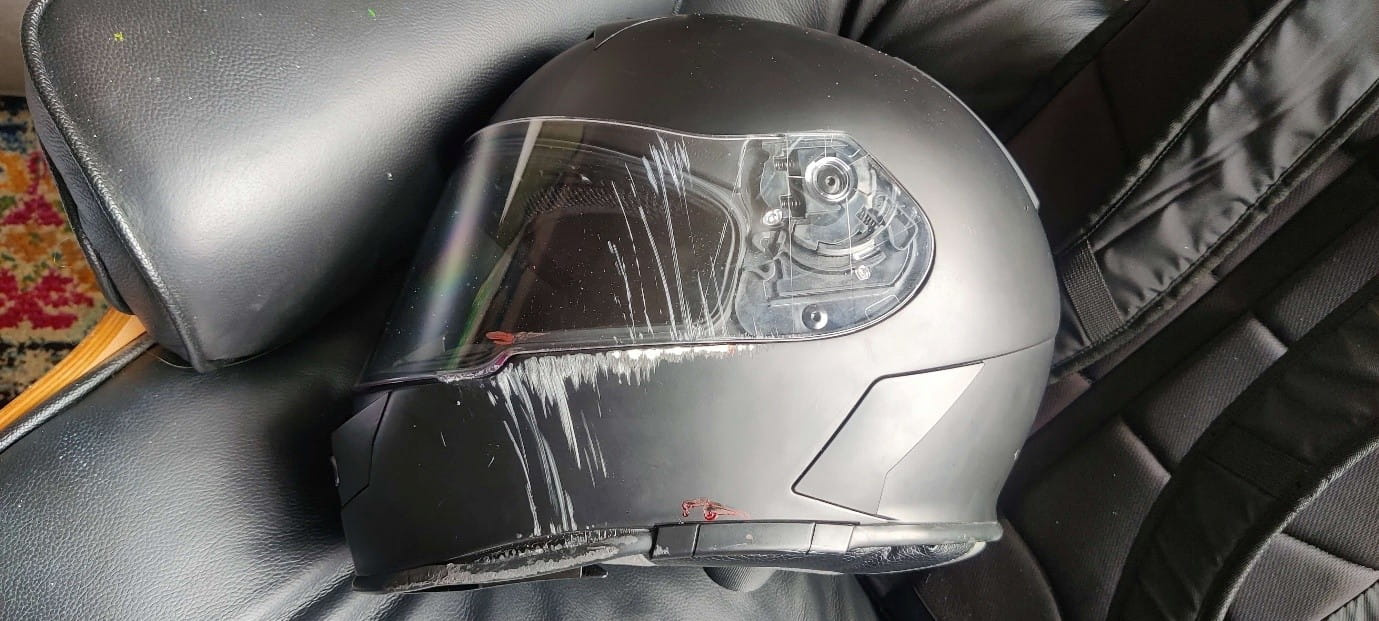 A close-up of a black motorcycle helmet showing heavy scuffs and impact damage on the visor and side.