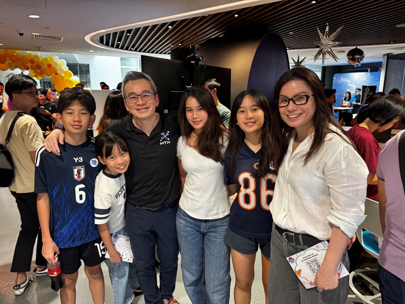 A family of six posing indoors at a social event with decoration and other attendees in the background.