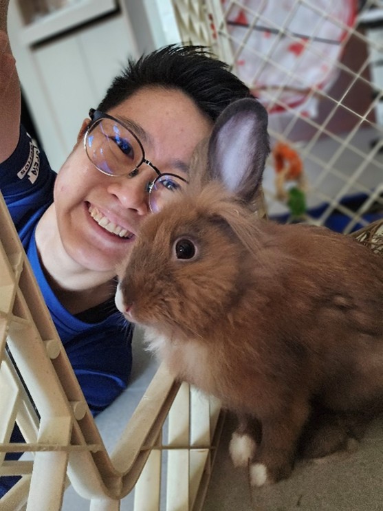 A selfie of a smiling lady leaning in next to a brown rabbit.