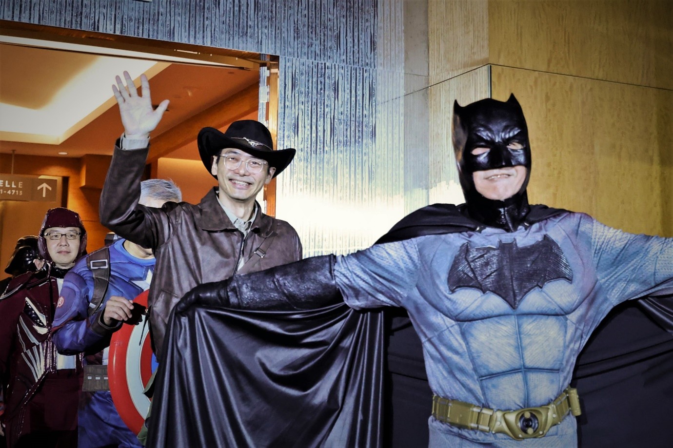 A few people entering a room, one dressed as Indiana Jones and another as Batman.