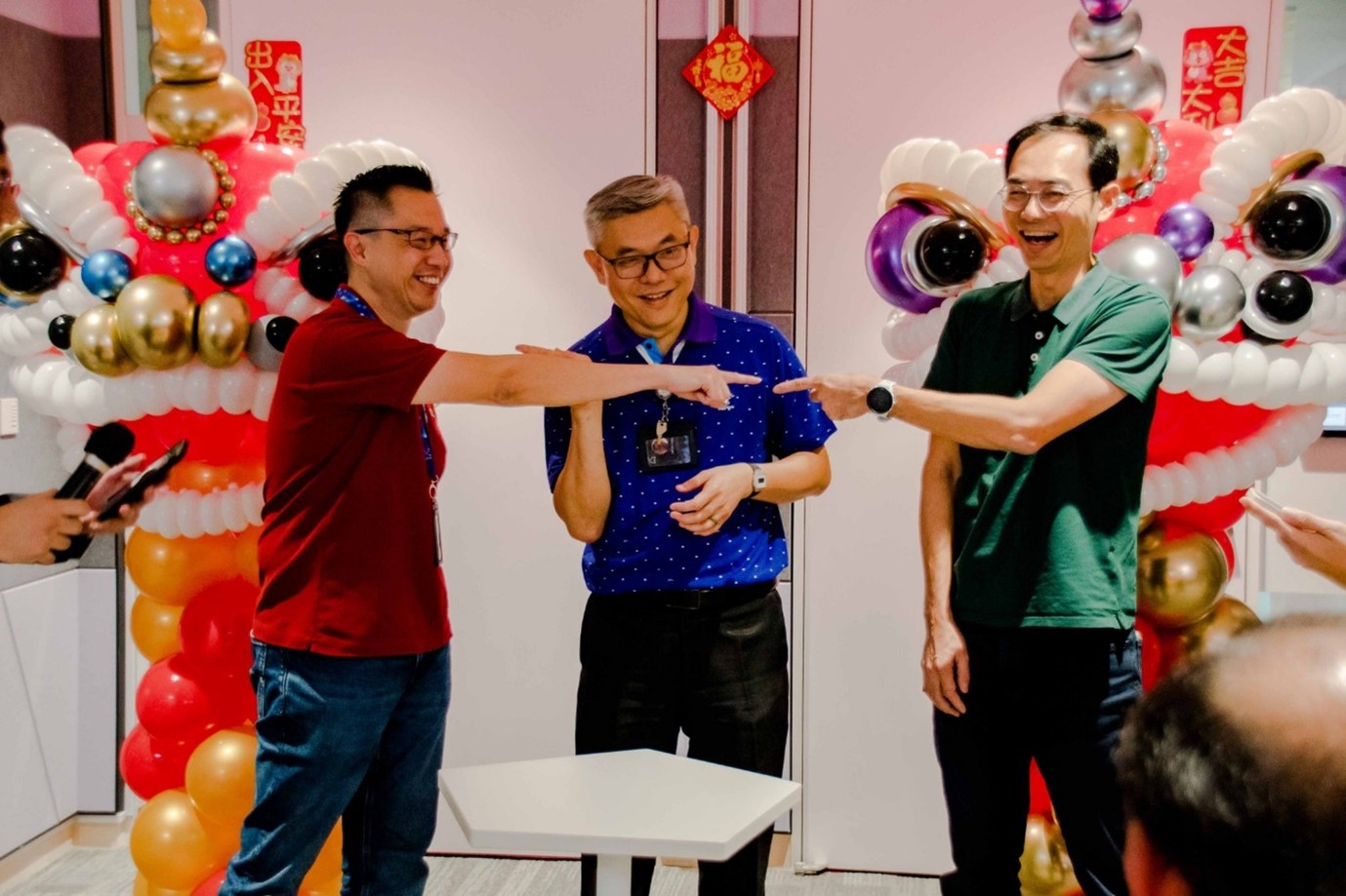 A group of men pointing at each other and laughing in front of bright decorations.