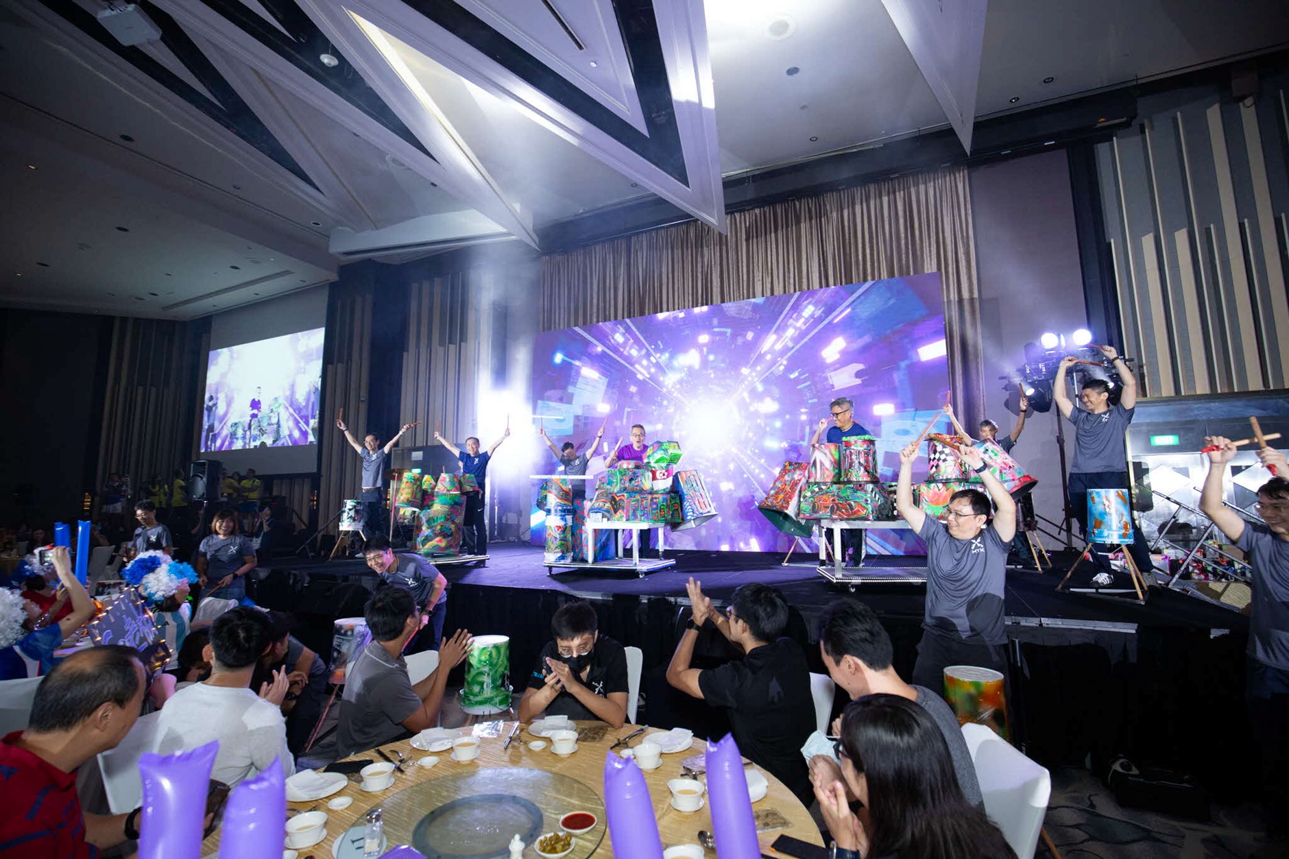 A group of people on a stage with their arms raised above drums.
