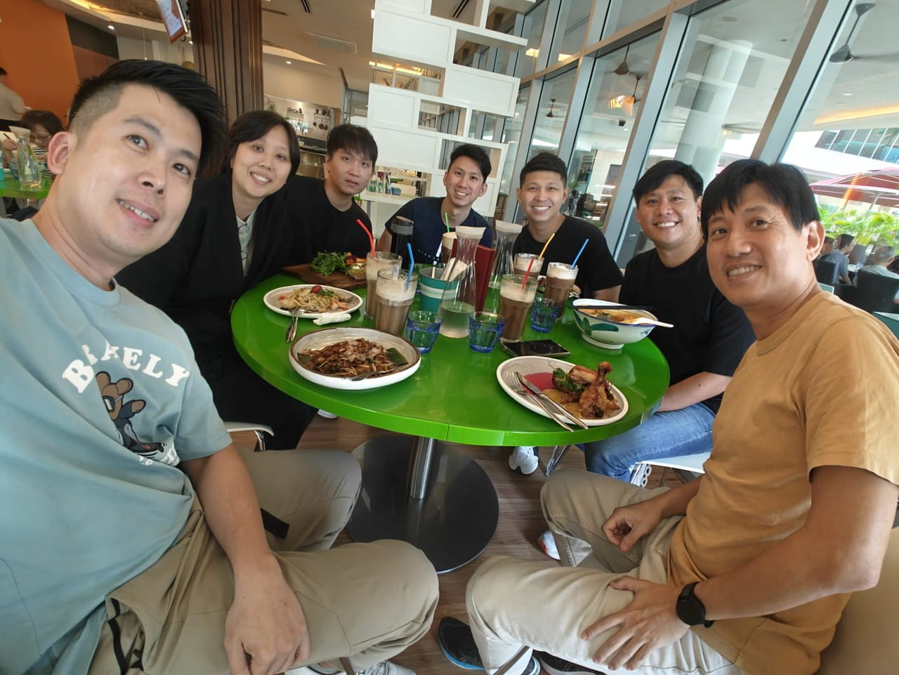 Group of people sitting around a green circular table in a restaurant.