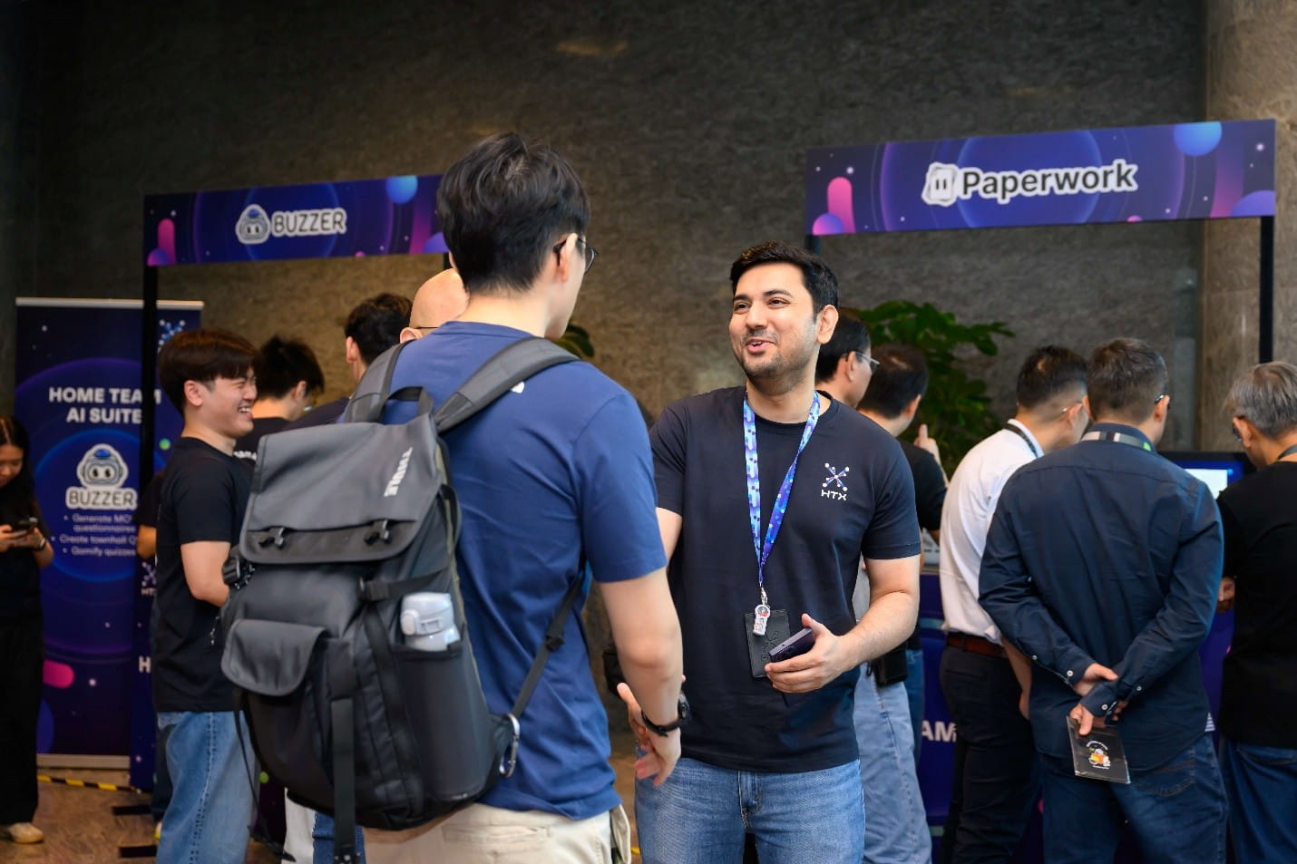 An event space featuring booths for "Buzzer" and "Paperwork," where attendees are interacting and networking.