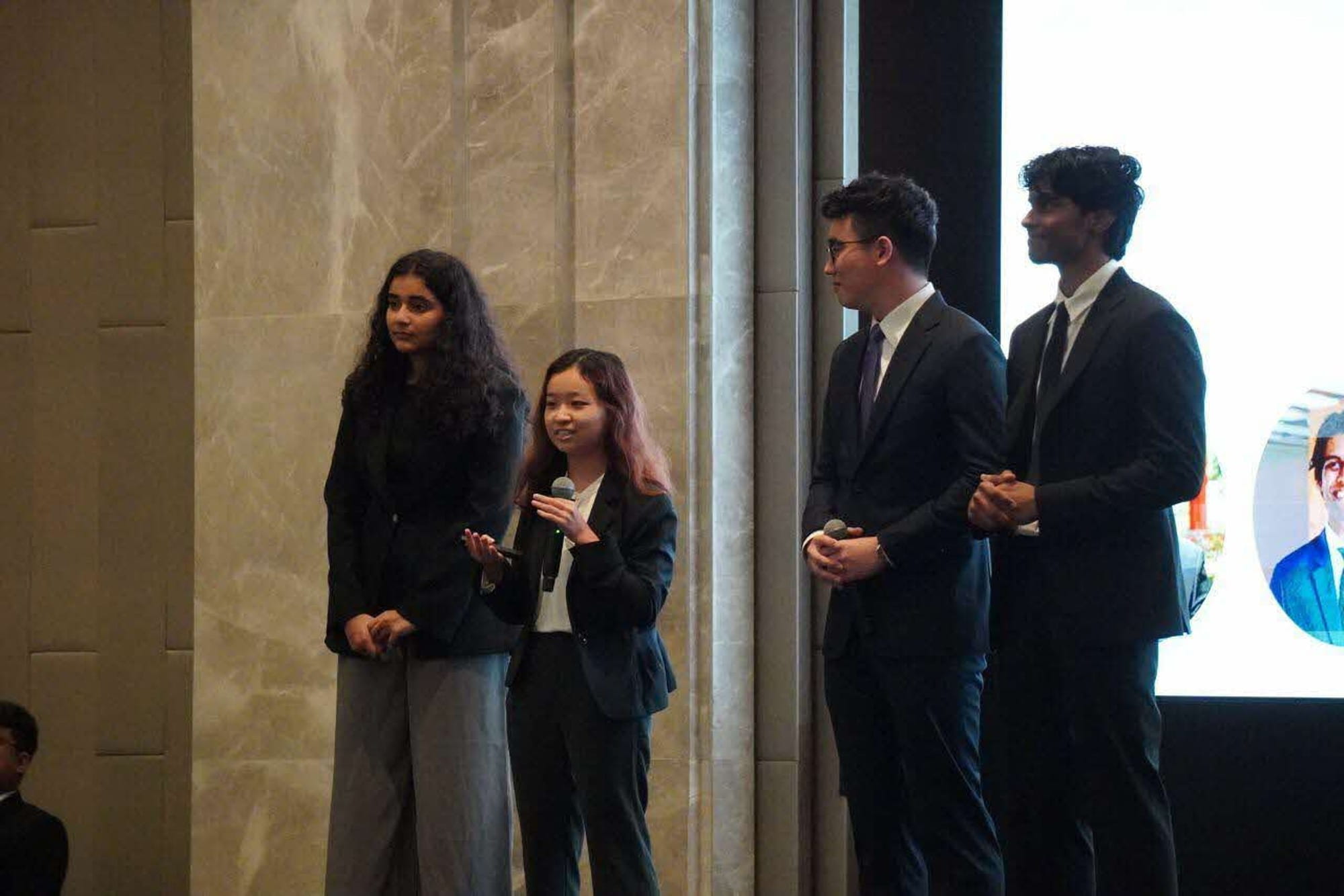 Four young professionals stand on stage during an event, dressed in formal attire.