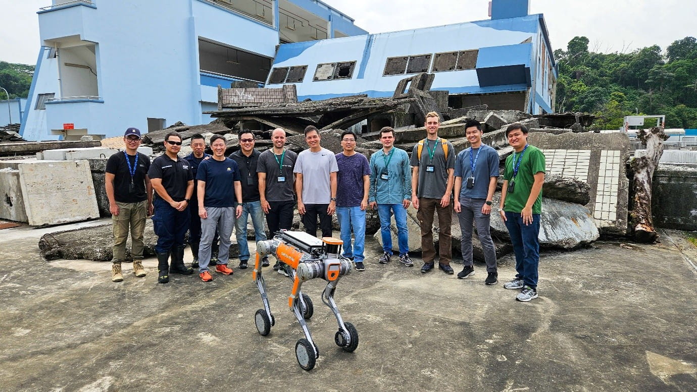 Group posing with a four-wheeled robotic dog in an outdoor concrete area.