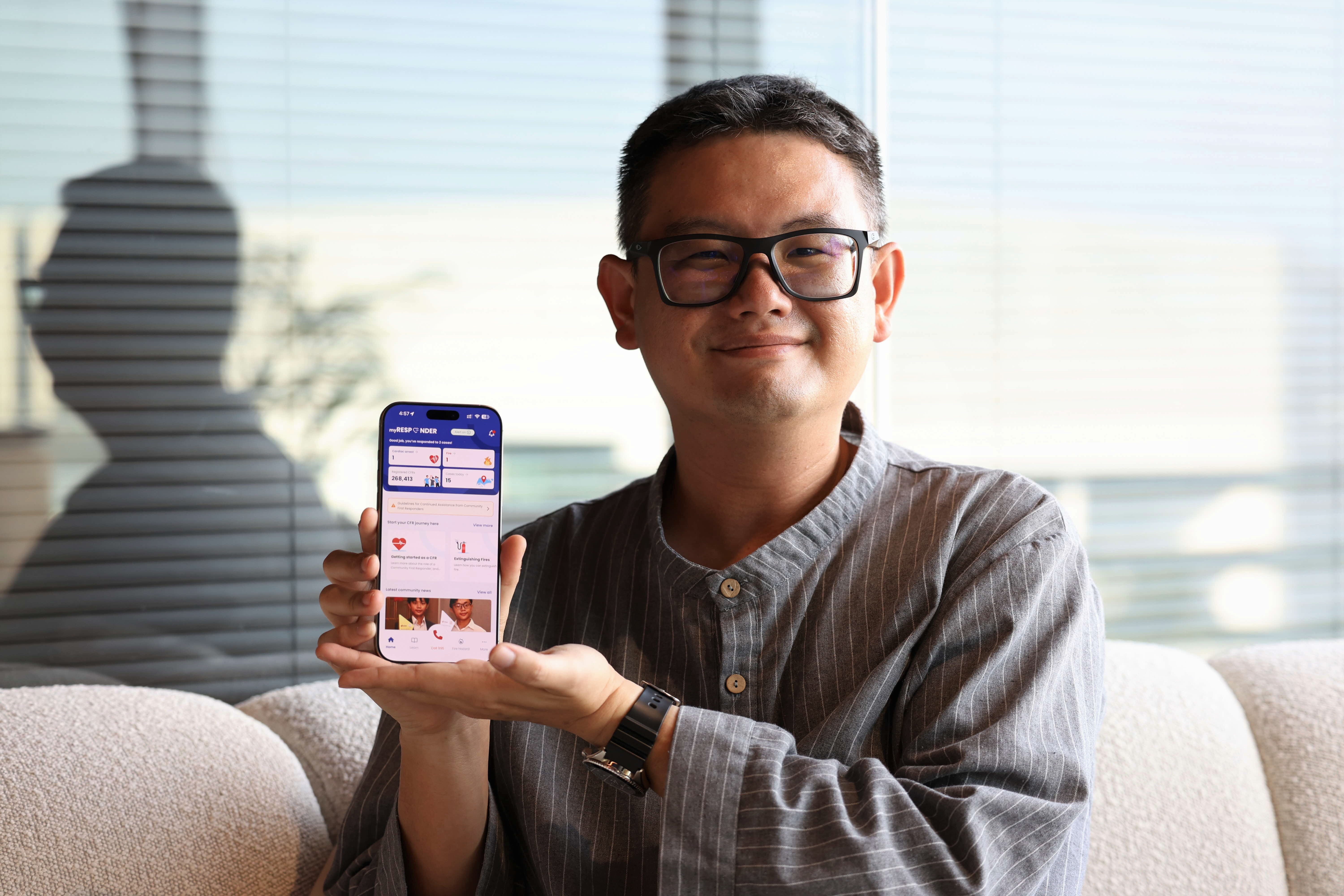 A man sitting on a couch holding a smartphone displaying a mobile app interface.