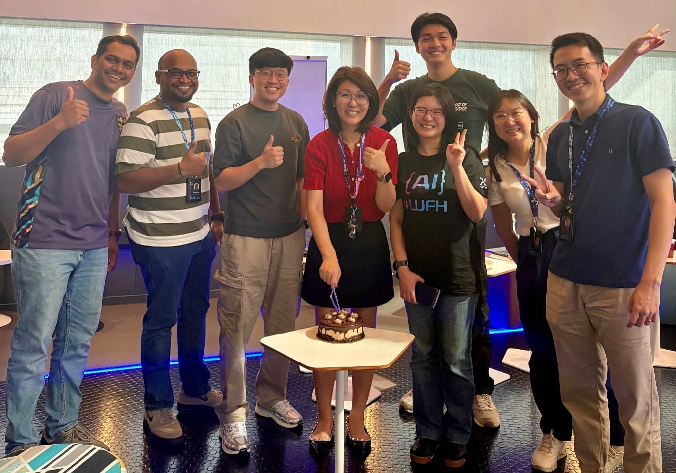 A group of people standing around a small table with a cake, celebrating an occasion indoors.